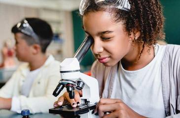 young school aged child using microscope in lab