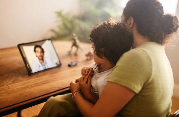 Mother and child video calling their family doctor at home stock photo